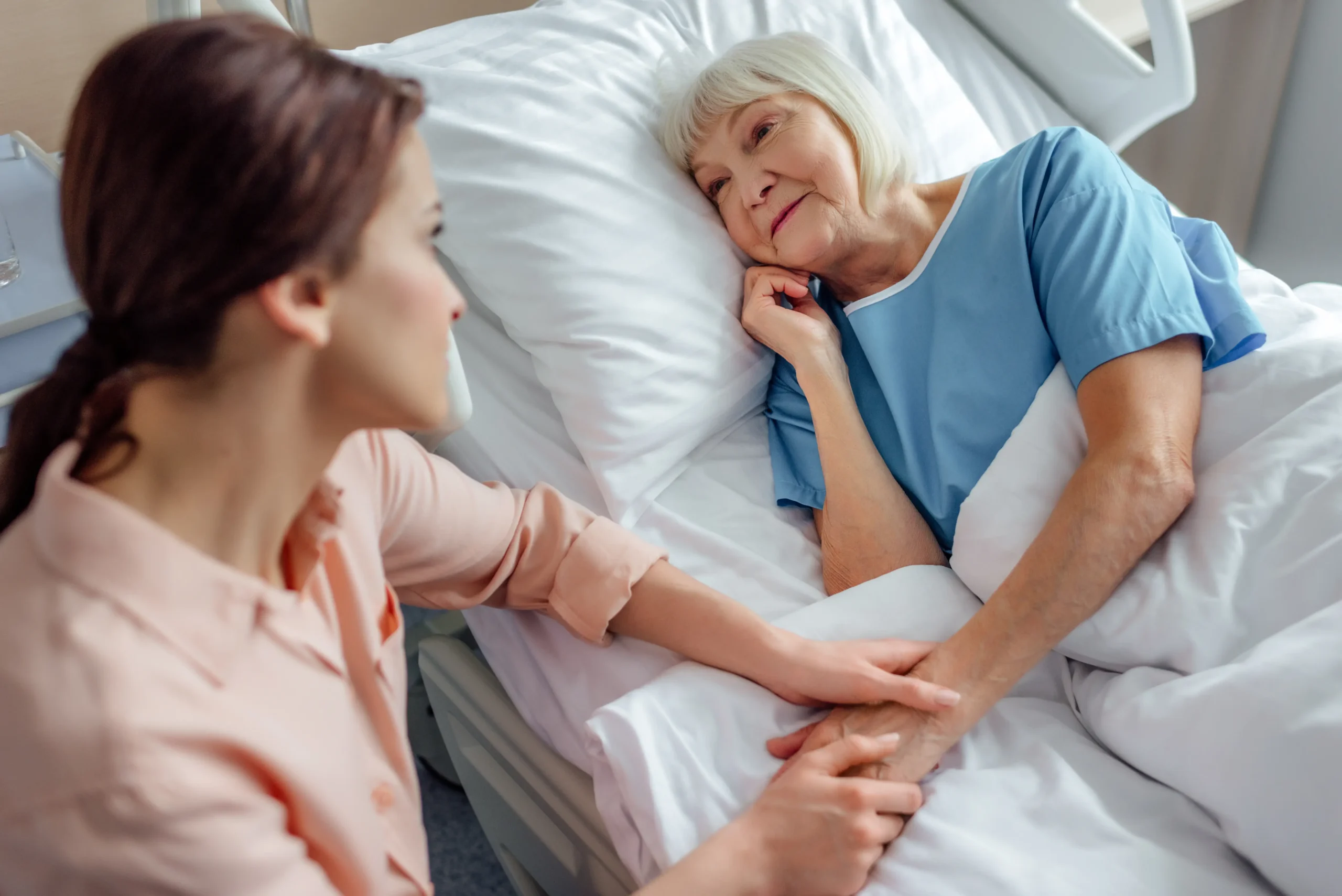 Daughter holding hands with her senior mother resting in bed